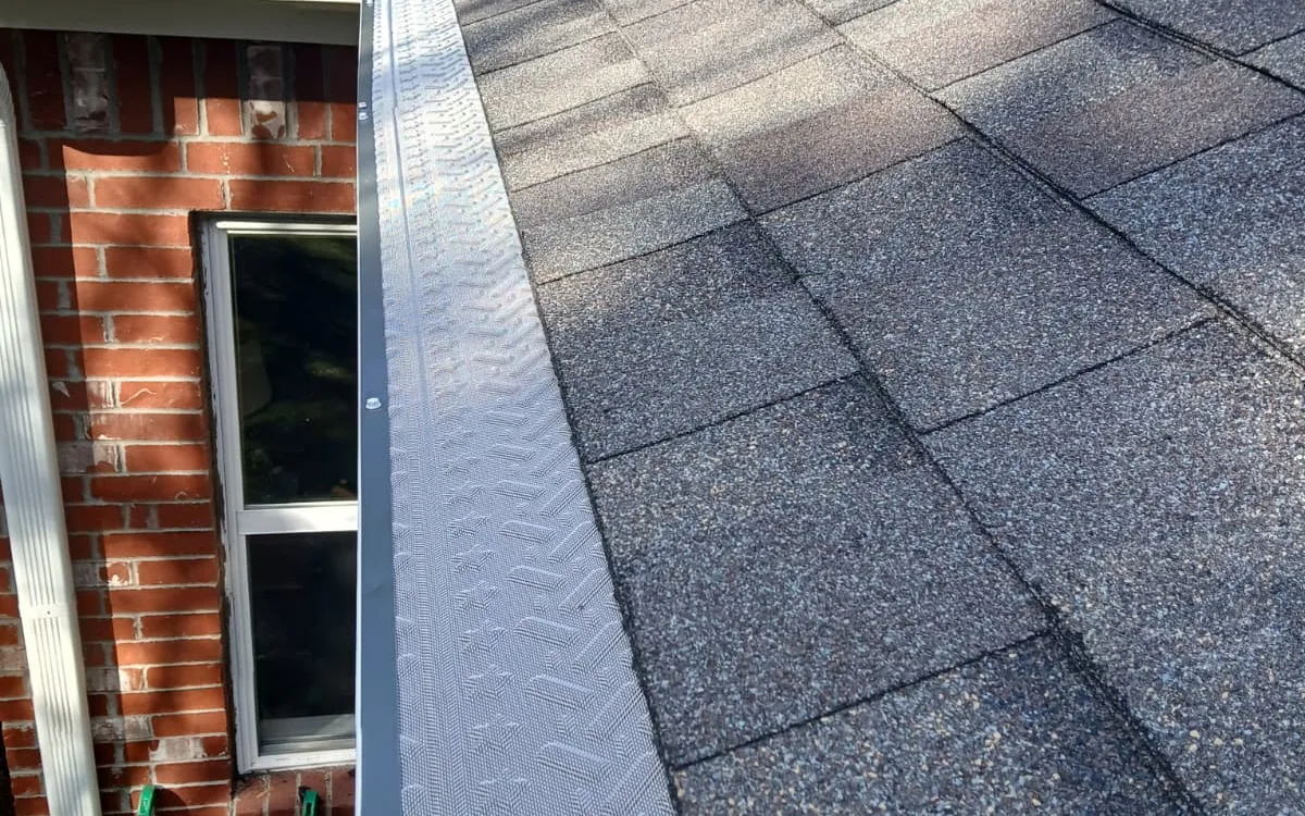 Gutter guard installed along a shingle roof edge above a red brick wall